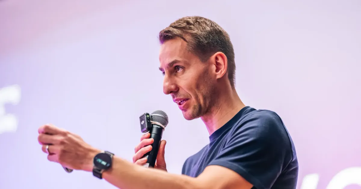 An engineering leader mid-sentence with a microphone, one hand reaching out to the room, at ELC meetup #43 in Prague.