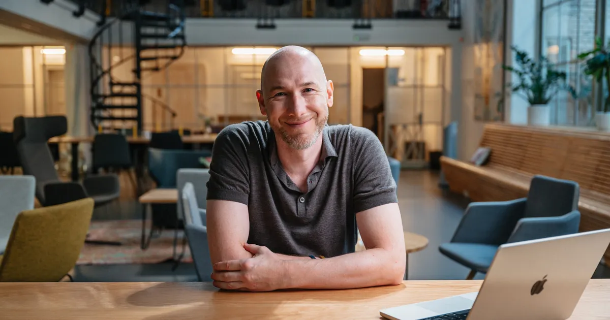 Marian Kamenistak at a desk in a coworking space, smiling, arms folded.