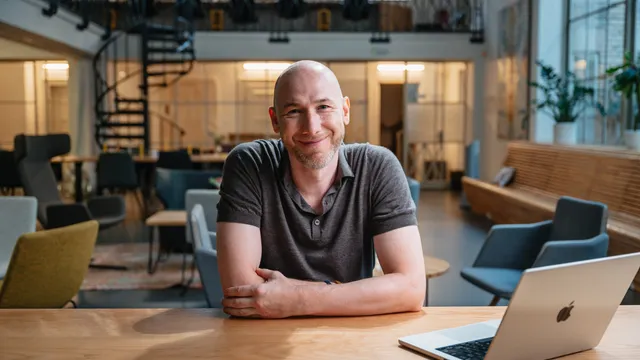 Marian Kamenistak at a desk in a coworking space, smiling, arms folded.