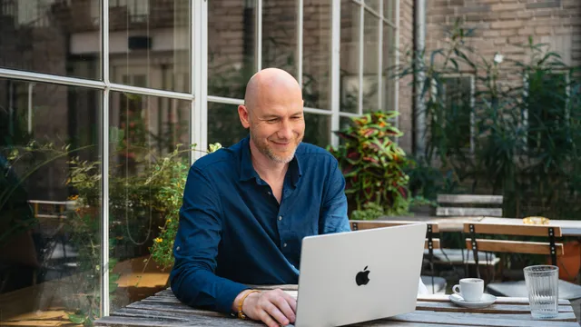 Marian Kamenistak smiling at his laptop in an outdoor courtyard.