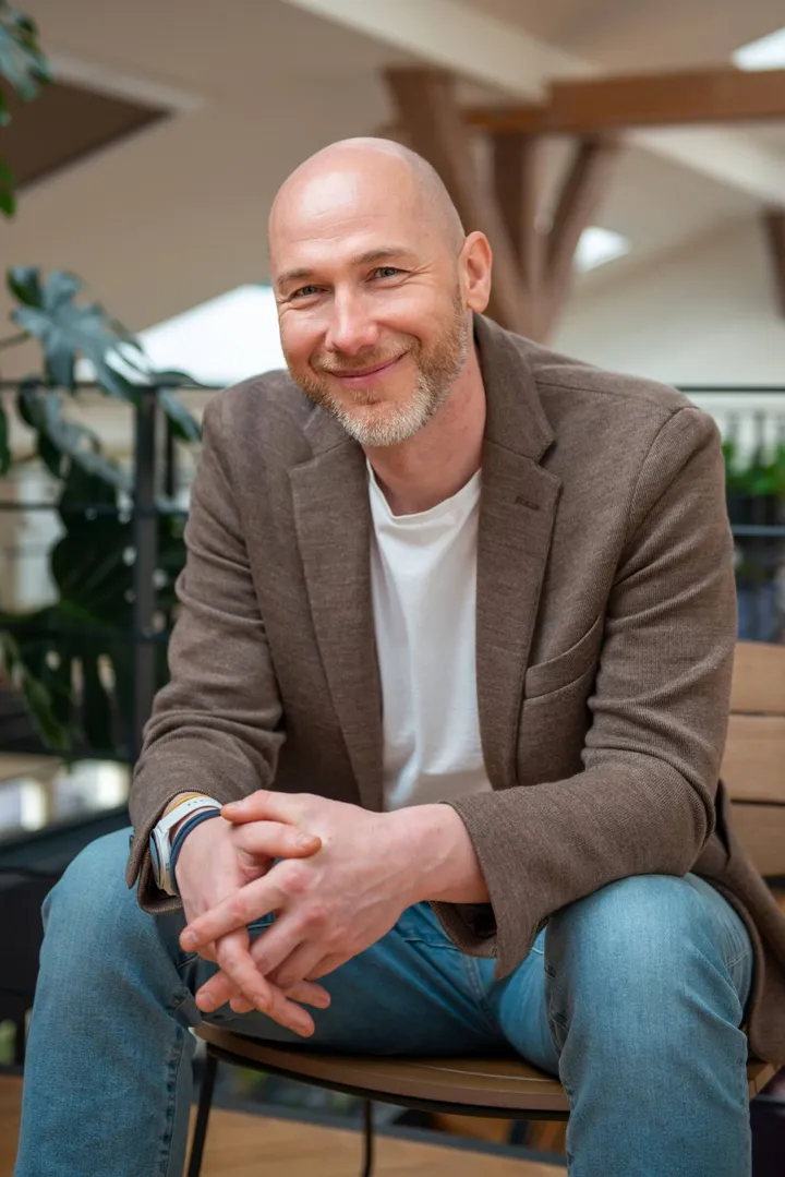 Marian Kamenistak sedí nakloněný dopředu se sepnutýma rukama, usmívá se.