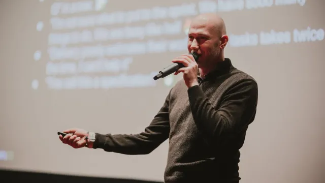Marian Kamenistak uprostřed přednášky, za ním promítnutý slide s odrážkami.