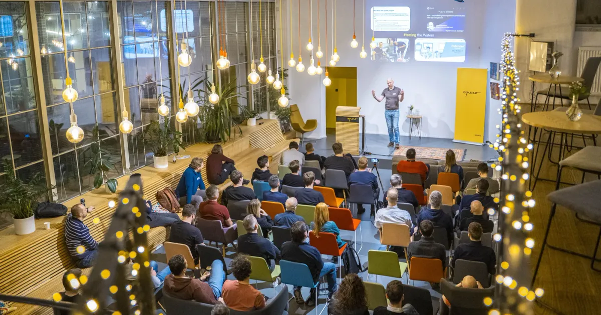 Wide shot of Marian Kamenistak speaking to a seated audience in a light-strung venue.