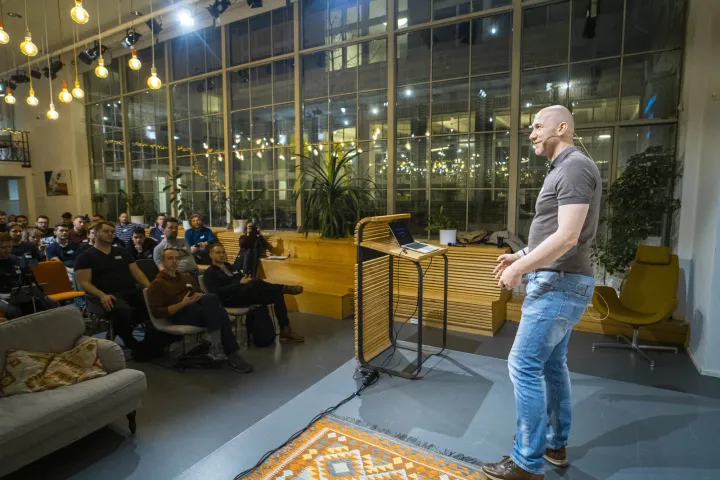 Marian Kamenistak presenting from a lectern in a glass atrium event space.