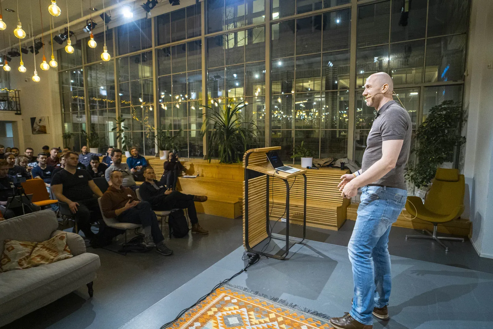 Marian Kamenistak presenting from a lectern in a glass atrium event space.