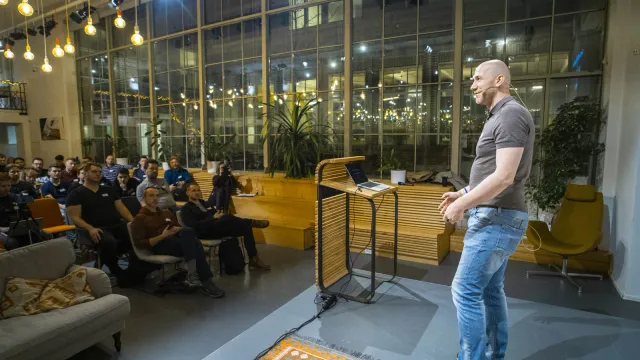 Marian Kamenistak presenting from a lectern in a glass atrium event space.