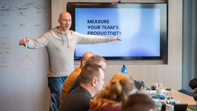 Marian Kamenistak leading a workshop in front of a screen reading "Measure your team's productivity" with strategy notes on the whiteboard.