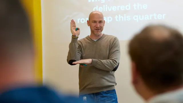 Marian Kamenistak facilitating a workshop, mid-gesture, in front of a slide about roadmap delivery.