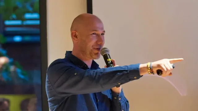 Marian Kamenistak speaking into a microphone at a meetup, pointing at the audience.