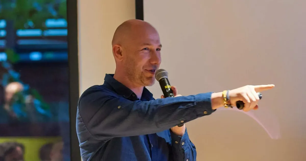 Marian Kamenistak speaking into a microphone at a meetup, pointing at the audience.