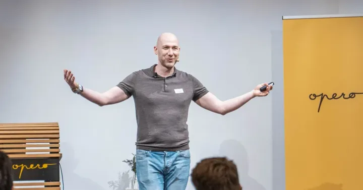 Marian Kamenistak on stage with arms spread wide, presenting to a meetup audience.