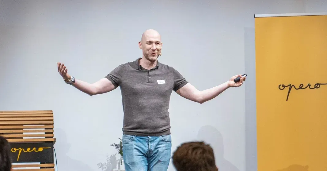 Marian Kamenistak on stage with arms spread wide, presenting to a meetup audience.