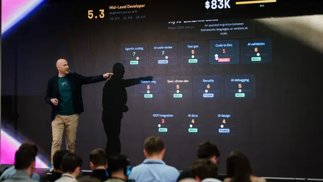 Marian Kamenistak pointing at a slide scoring AI-assisted engineering skills — agentic coding, AI code review, MCP integration — against a mid-level developer salary.
