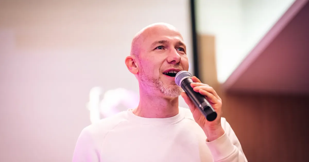 Marian Kamenistak mluví do mikrofonu na meetupu ELC #43, uprostřed věty, v krémovém svetru.