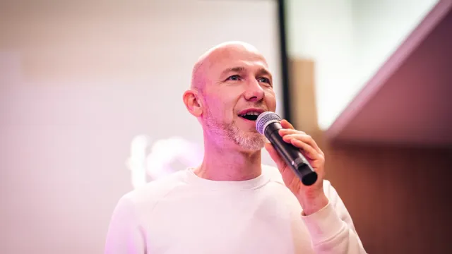 Marian Kamenistak mluví do mikrofonu na meetupu ELC #43, uprostřed věty, v krémovém svetru.