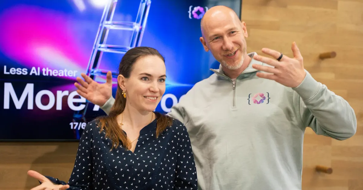 Marian Kamenistak gestikuluje vedle usměvavé hostky před obrazovkou s nápisem „Less AI theater“ na meetupu ELC.