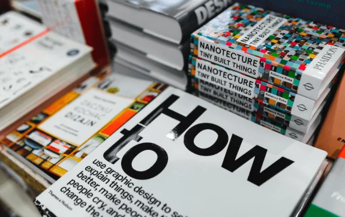 Stack of design books on a table, the top one titled How to use graphic design to sell things