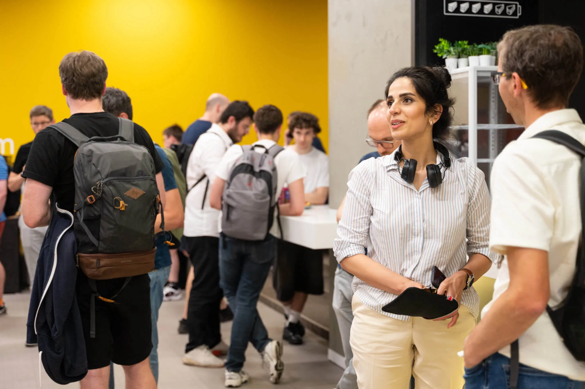 A woman with headphones round her neck talking to an attendee while the meetup crowd queues for refreshments