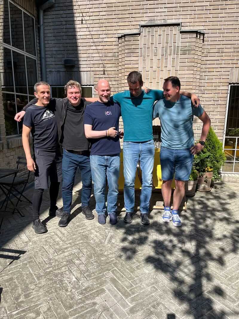 Five course participants standing arm in arm in a sunlit brick courtyard during a break