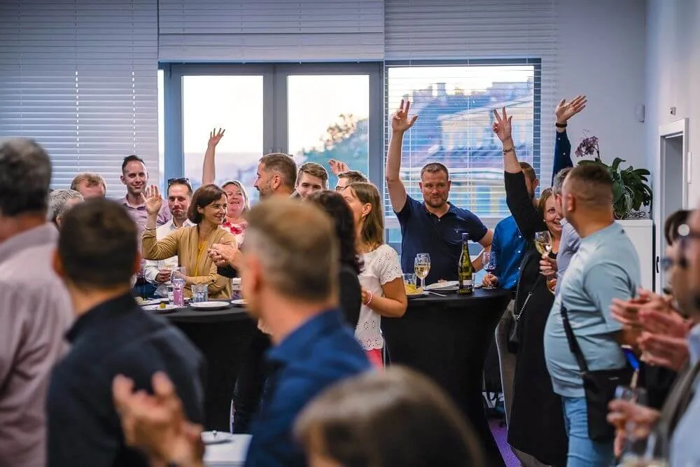 Guests at a company evening raising hands and applauding around cocktail tables with wine glasses