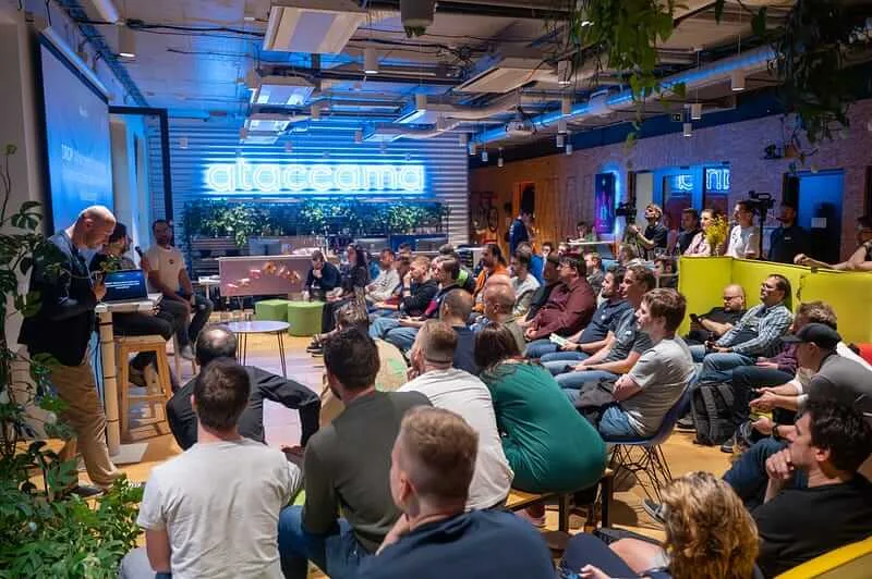 A packed ELC meetup at the Ataccama office, a speaker standing at a laptop under the neon Ataccama sign
